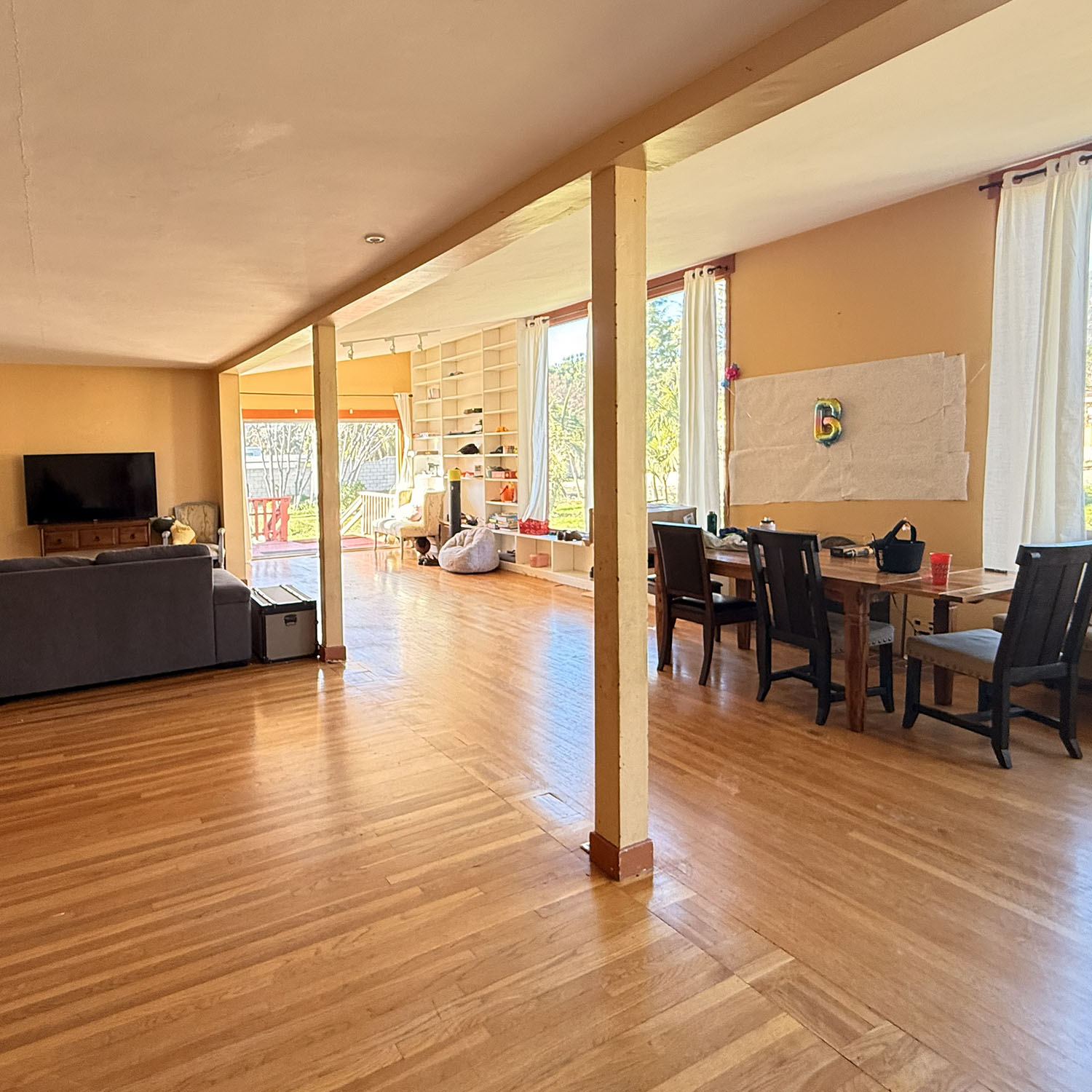 The same living and dining space before the remodel — dated yellow walls, worn hardwood and a structural post — Mediterranean Estate, Pasadena