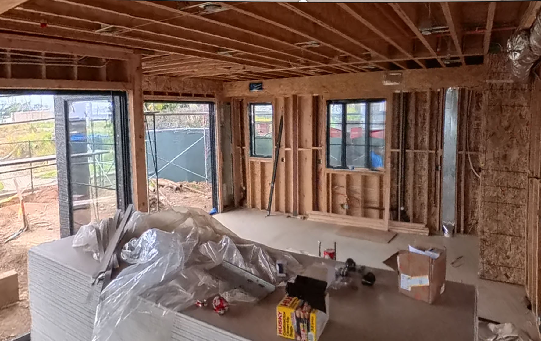 The same great room and kitchen during construction — framed studs, subfloor and open windows — Pacific Palisades fire rebuild by Vividly Built