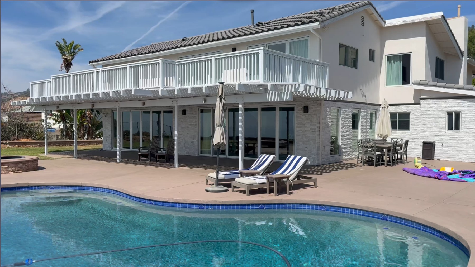 The same Palos Verdes home photographed before the remodel — original tile hip roof, full-length white balcony railing, striped patio awnings and a kidney-shaped pool